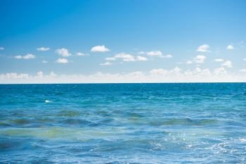 Seascape with blue water surface, calm waves, bright sky and white clouds