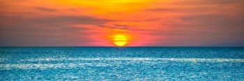 Panorama of nature landscape with beautiful dramatic orange sunset over blue rippled sea