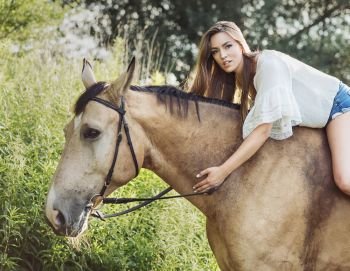 Portrait of the cute brunette woman riding a brown horse