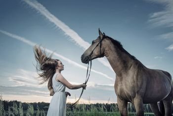 Blond young woman playing with a majestic horse