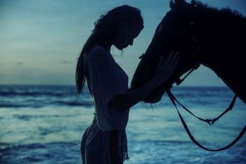 Pretty brunette woman with her horse over the sunset