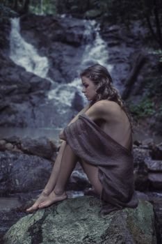 Portrait of a young woman meditating by the waterfall