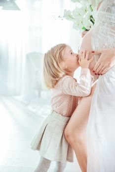 Little daughter kissing her pregnant mother’s belly
