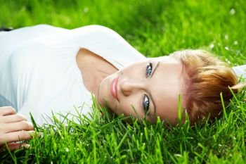 Portrait of beautiful young woman lying on a fresh green lawn