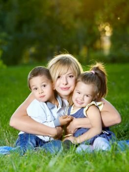 Mother embraces two children on a summer lawn