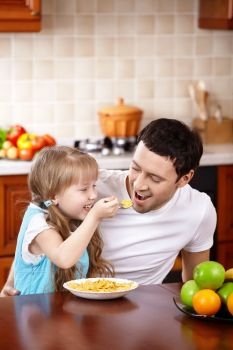 The little girl spoon-feeds the daddy on kitchen
