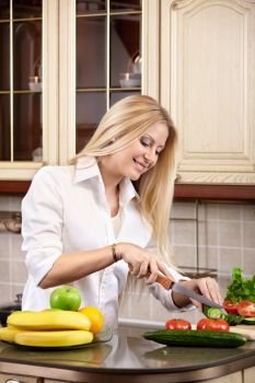 The attractive girl cuts vegetables on kitchen