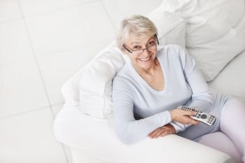 Mature attractive woman with a remote control from a TV on a white sofa