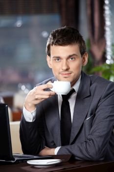 Business man with the laptop drinks coffee in cafe