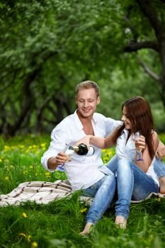 The attractive enamoured couple drinks champagne in park