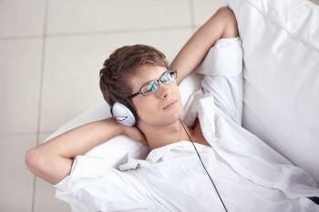 A young man listening the music in the headphones on the sofa