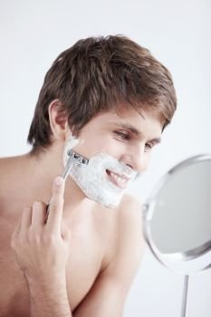 Young man shaving at the mirror