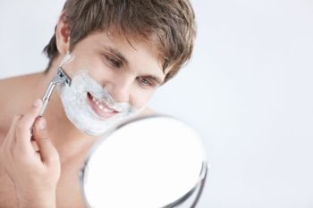 Young attractive man shaves in the mirror