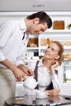 The young waiter pours tea to the client in cafe
