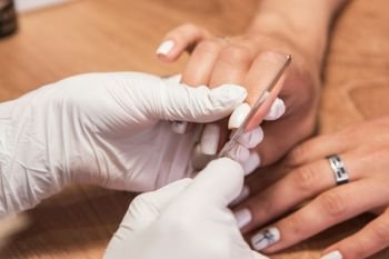 Closeup photo of a woman in a nail salon receiving a manicure by a beautician with nail file.. Woman in a nail salon