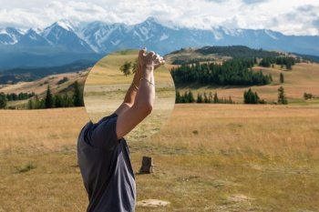 Man standing in in summer Altai mountains in Kurai steppe and holding circle mirror. Creative travel concept. Man standing in in summer Altai mountains