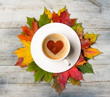 Fall in love. Coffee cup with heart symbol on autumn colorful leaves on wooden table, top view. Fall in love. Autumn coffee and leaves