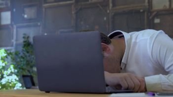 Tired businessman sleeping on a laptop in small business office for startup team.. Businessman sleeping on laptop