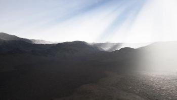 the sun’s rays against the backdrop of the mountains and the lava-rocky wet shore in the foreground. Sun Rays against the Backdrop of the Mountains