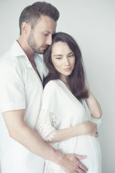 Lifestyle portrait of handsome young happy man hugging his beautiful pregnant wife. Family photo. Love and care