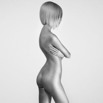 black-and-white portrait of beautiful nude woman with sexy body. Studio photography of young naked lady on grey background. Pretty blonde with perfect figure. Professional hair-dress and makeup.