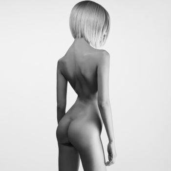 black-and-white portrait of beautiful nude woman with sexy body. Studio photography of young naked lady on grey background. Pretty blonde with perfect figure. Professional hair-dress and makeup.