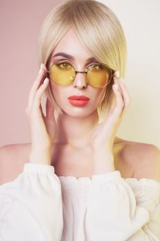 Beautiful sexy blonde with professional classic make-up pose in photography studio. Sensual stylish woman in erotic white dress. Blue-eyed lady with perfect lips in modern colour sunglasses