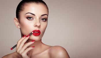 Beautiful Woman paints Lips with Lipstick. Beautiful Woman Face. Makeup detail. Beauty Model with Perfect Skin. Red Lips and Nails Manicure