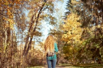 A young red-haired woman walks through the autumn park. A girl with lush curly hair looks at the autumn forest