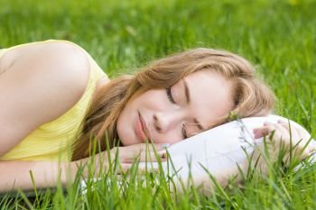 Young woman sleeping on white pillow in fresh spring grass. Woman sleeping on grass