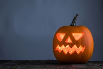 Glowing Halloween pumpkin head jack lantern on wooden table. Glowing Halloween pumpkin