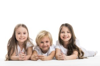 Happy smiling three children in white clothes laying on floor isolated on white background. Happy children isolated on white