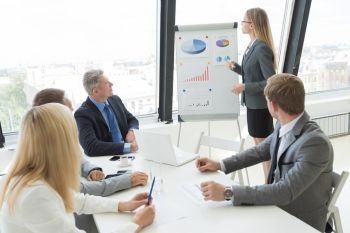 Businesswoman giving a presentation to her colleagues at work standing in front of a flipchart with diagrams. Business woman giving a presentation