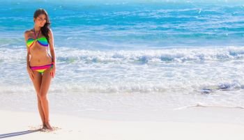 Happy tanned girl in rainbow bikini at seaside, blue sea water in background. Happy girl in bikini at seaside