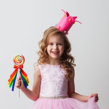 Beautiful little candy princess girl in crown holding big lollipop and smiling. Candy princess girl with lollipop