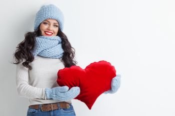 Beautiful woman in warm winter clothes with a big red heart shape pillow , copy space for text , Valentines day , love winter concept. Woman with red heart shape pillow