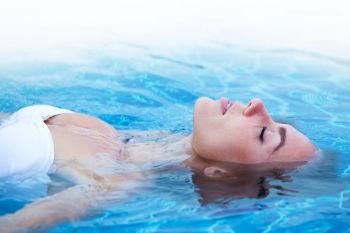 Girl in bikini relaxing floating in blue water of swimming pool. Girl relaxing in swimming pool