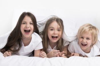Happy three children under one blanket isolated on white background. Children under blanket