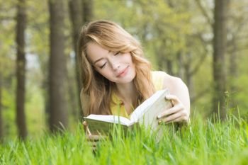 Pretty girl laying on the grass and reading a book in spring park and smiling. Girl reading book on grass