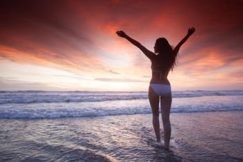 Woman in bikini raising arms towards beautiful glowing sunset over sea. Woman at sea sunset