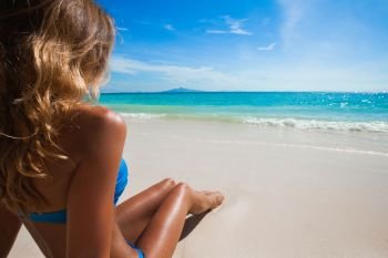 Woman on beach sitting in sand looking at ocean enjoying sun and summer travel holidays vacation getaway. Girl in bikini relaxing under blue sky.. Woman on beach looking at ocean