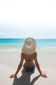 Woman in bikini and sunhat sitting on beach and looking at sea. Woman in sunhat on sea beach
