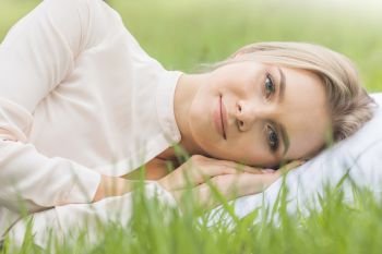 Young cute girl resting on soft pillow in fresh spring grass. Girl resting on soft pillow