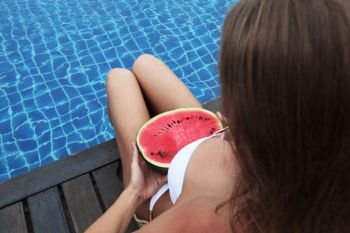 Beautiful woman with fit, tanned body in bikini with watermelon tanning poolside. Woman with watermelon poolside