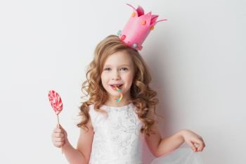 Beautiful little candy princess girl in crown holding big pink heart lollipop and candy cane. Little candy princess
