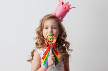 Beautiful little candy princess girl in crown holding big lollipop and smiling. Girl in crown holding lollipop