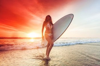 Silhouette of woman on tropical beach holding surfboard at sunset in Bali. Woman holding surfboard at sunset