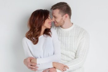 Happy smiling couple dressed in white hugging and looking to each other on white background, love, relations, Valentines day concept. Happy couple ib white hugging