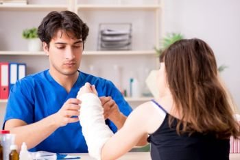 Young woman with bandaged arm visiting male doctor traumotologist . Young woman with bandaged arm visiting male doctor traumotologis