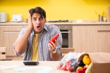 Young man calculating expences for vegetables in kitchen 